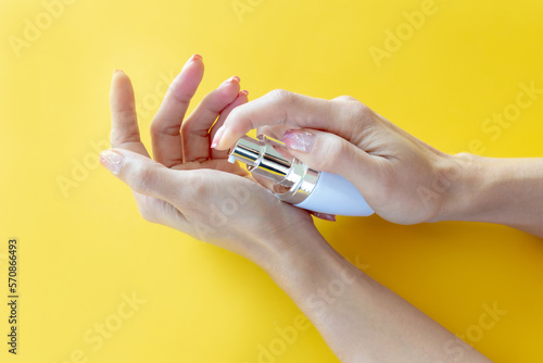 Female's hand holding product of glass bottle with dropper lid on yellow background.Packaging product of cream,lotion,gel, foam or skincare.Cosmetic and medicine product branding mockup.Copy space.