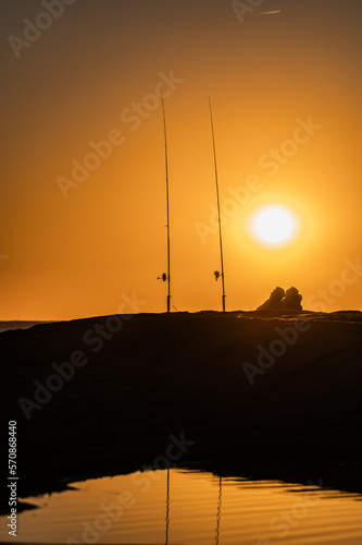 Silhouette of fishermen and fishing rods, with the sunset and the sun sphere in the background. Castelldefels, Barcelona, Spain