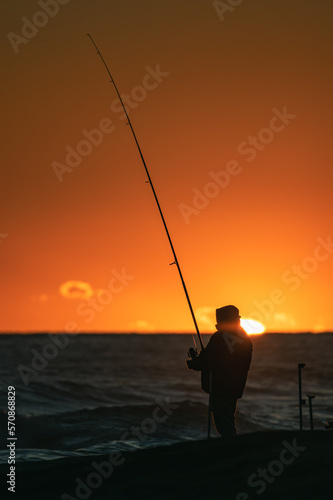 Silhouette of fishermen and fishing rods, with the sunset and the sun sphere in the background. Castelldefels, Barcelona, Spain