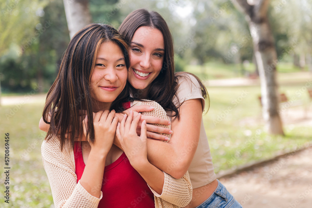 Naklejka premium couple of happy women looking at camera embracing and smiling during a date in a park, concept of friendship and love between people of the same sex, copy space for text