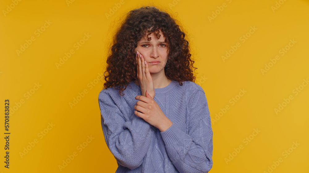 Hipster curly haired woman touching sore cheek suffering from toothache cavities or gingivitis waiting for dentist appointment gums disease. Young girl indoor studio shot isolated on yellow background Hipster curly haired woman touching sore cheek suffering from toothache cavities or gingivitis waiting for dentist appointment gums disease. Young girl indoor studio shot isolated on yellow background