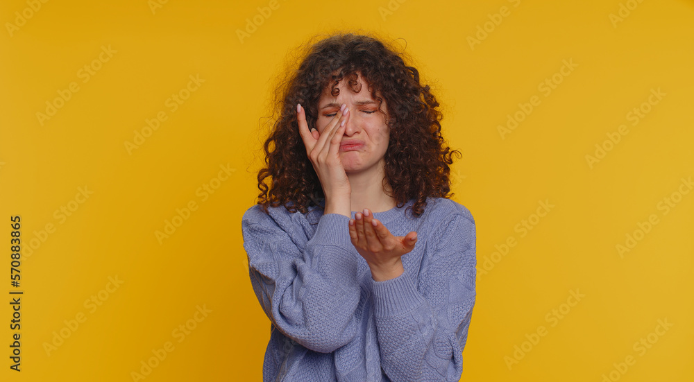 Upset disappointed young curly haired woman wipes tears and cries from despair, being sad because of unfair things. Teen girl in depression, despair, loss isolated alone on yellow studio background Upset disappointed young curly haired woman wipes tears and cries from despair, being sad because of unfair things. Teen girl in depression, despair, loss isolated alone on yellow studio background