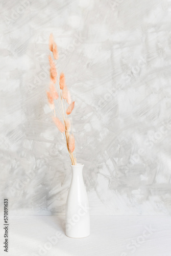 Fototapeta Naklejka Na Ścianę i Meble -  bunch of dried bunnytail flower (Lagurus ovatus) in a white ceramic vase on a table with a white linen tablecloth. Simple and minimal home decoration. Gray wall, copy space.