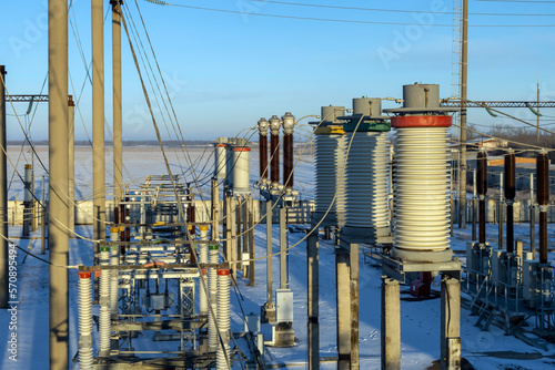 Part of a high-voltage substation against a blue sky with switches and disconnectors in the rays of the morning winter sun.