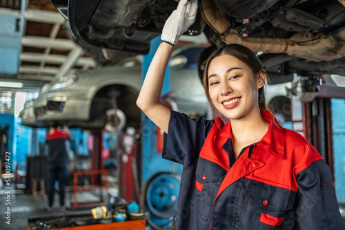Asian automotive engineer people wear helmet work in mechanics garage.young auto mechanic in uniform is looking at camera and smiling examining car.