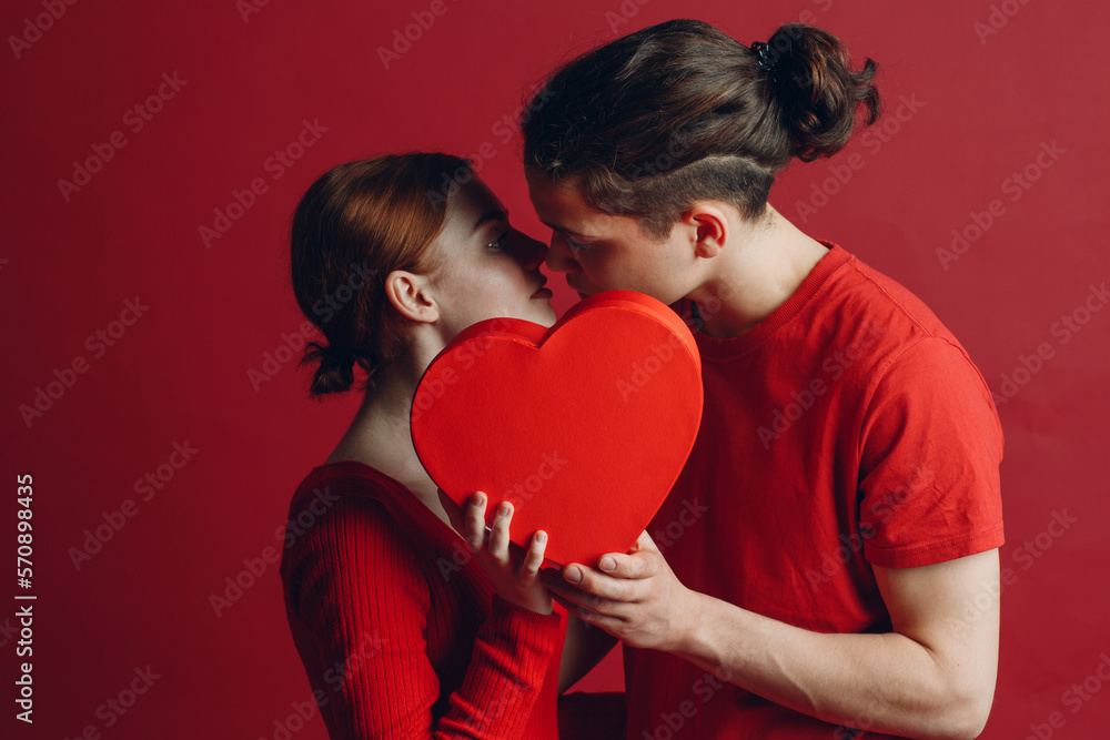 Man and woman young couple kissing and hiding behind heart-shaped box. Man and woman young couple kissing and hiding behind heart-shaped box.