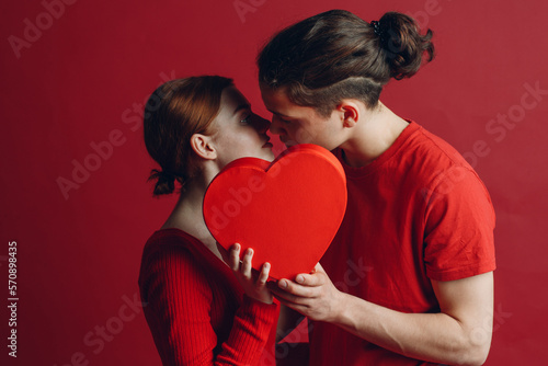 Man and woman young couple kissing and hiding behind heart-shaped box.