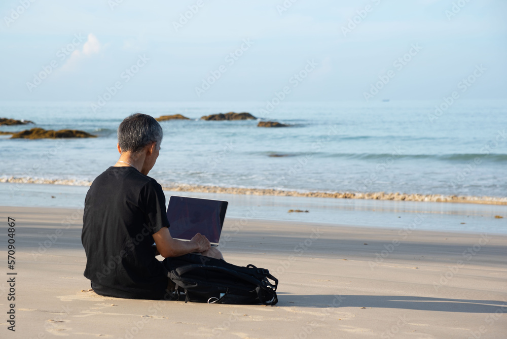 A senior adult using computer on the beach