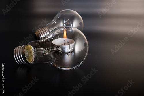 Electric lamp and candle on a dark background.  Incandescent bulb and candle. Power cut or power outage. High electricity prices. Saving electricity. Symbol of return to the past.
