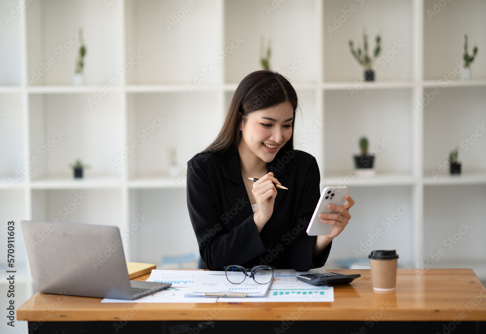 Young smart Asian businesswoman working at the working table and using her smartphone at the same time. Young smart Asian businesswoman working at the working table and using her smartphone at the same time.