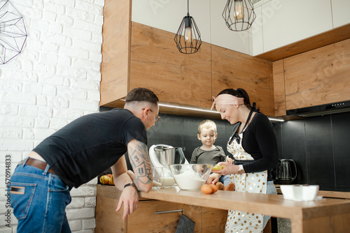 Laughing, merry delightful woman, man and little blond boy baking together in kitchen. Little child watching mother cook photo