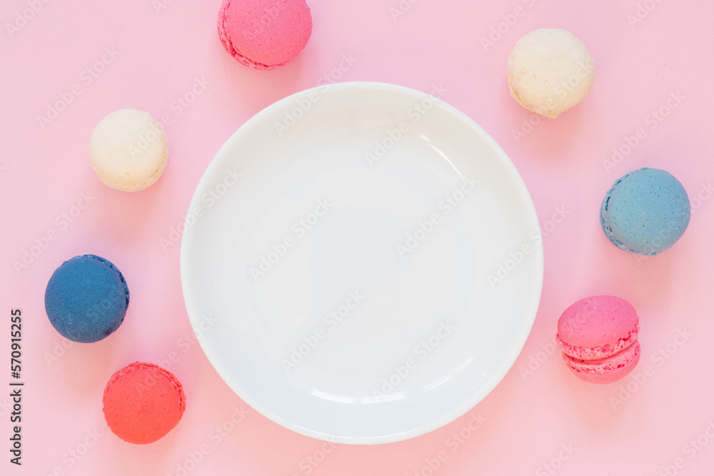 Empty white plate on pink background, colorful macaroon cookies around it. Girly, romantic colors Empty white plate on pink background, colorful macaroon cookies around it. Girly, romantic colors