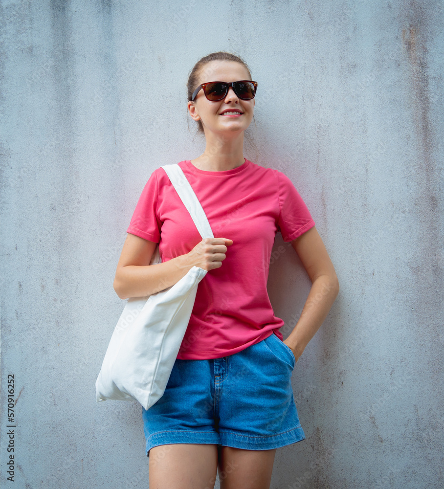 Female model wearing pink blank t-shirt on the background of an gray wall.