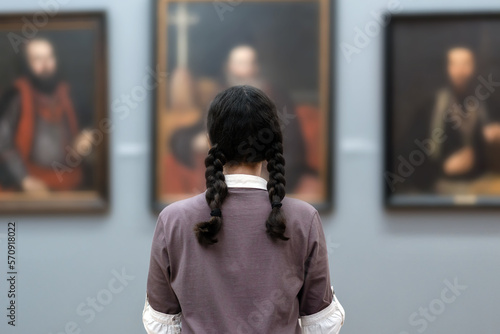 Back view of young woman contemplates ancient pictures. Student visiting arts exhibition. Museum day. Concept of modern culture education photo
