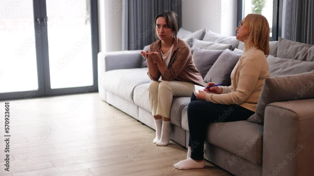Young sad woman is sitting on the couch, holding her hands to her face at a psychotherapist's appointment. Psychologist with a client Young sad woman is sitting on the couch, holding her hands to her face at a psychotherapist's appointment. Psychologist with a client