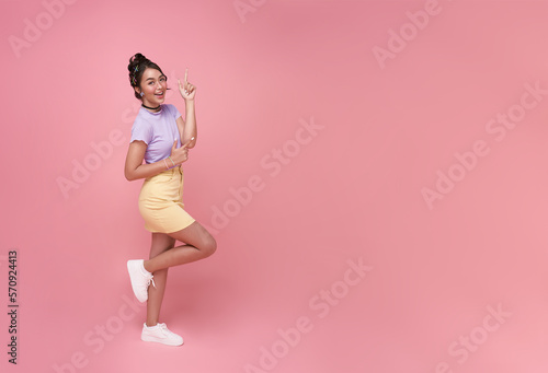 Happy young Asian teen woman standing with her finger pointing isolated on pink background with copy space.