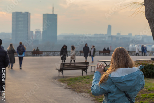 Belgrade, Serbia. February 11th, 2023. Girl taking a photo of a cityscape in the Kalemegdan park at sunset. photo