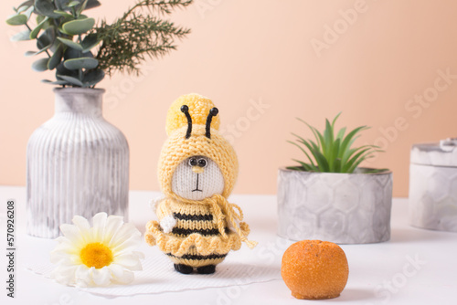 a knitted yellow bee sits on a white plate with a daisy. Handmade knitting toy, amigurumi gift for Children