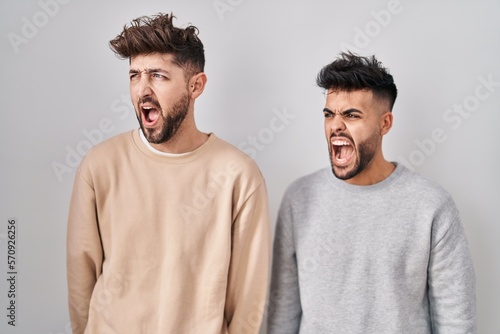 Young homosexual couple standing over white background angry and mad screaming frustrated and furious, shouting with anger. rage and aggressive concept.