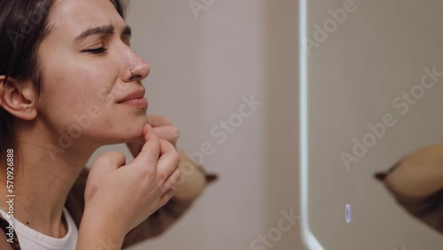 Displeased woman looking in mirror reflection squeezing acnes on skin face in bath room. Focused girl removing pimple on face. Problem skin care photo