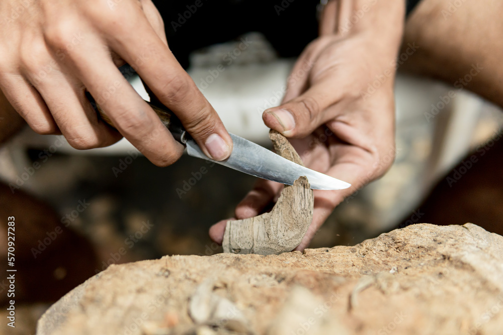 hands of young Latino man carving a figure in wood with knife