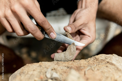 hands of young Latino man carving a figure in wood with knife