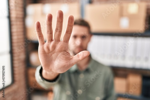 Young man ecommerce business worker doing stop gesture with hand at office photo