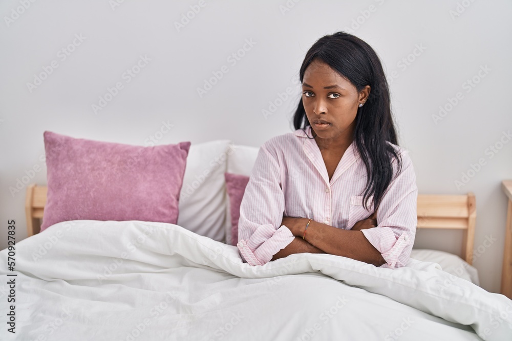 Young african american woman sitting on bed with serious expression and arms crossed gesture at bedroom
