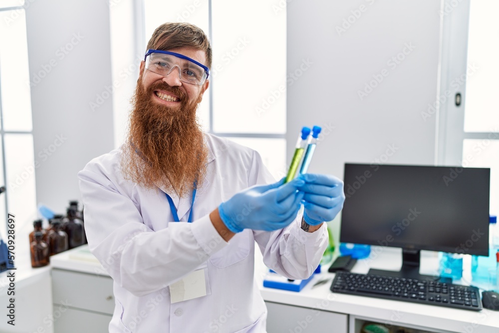 Young redhead man wearing scientist uniform holding test tubes at laboratory Young redhead man wearing scientist uniform holding test tubes at laboratory