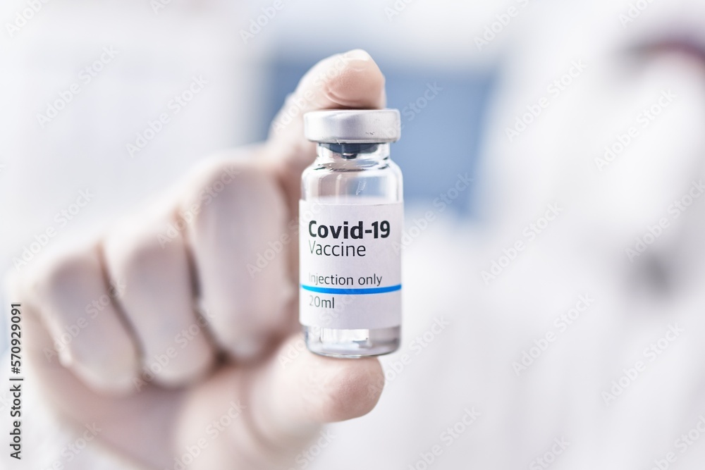 Young hispanic man scientist wearing medical mask holding covid vaccine dose at laboratory