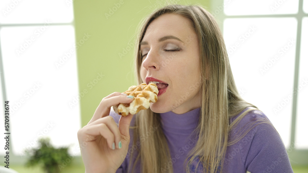 Young blonde woman eating waffle sitting on table at home Young blonde woman eating waffle sitting on table at home