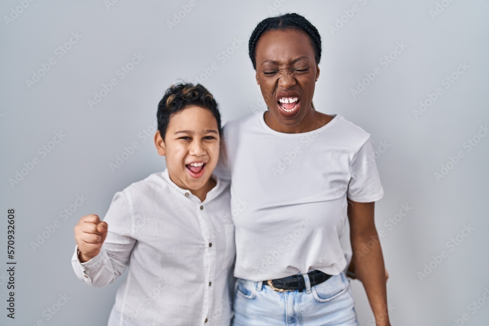 Young mother and son standing together over white background angry and mad screaming frustrated and furious, shouting with anger. rage and aggressive concept. Young mother and son standing together over white background angry and mad screaming frustrated and furious, shouting with anger. rage and aggressive concept.