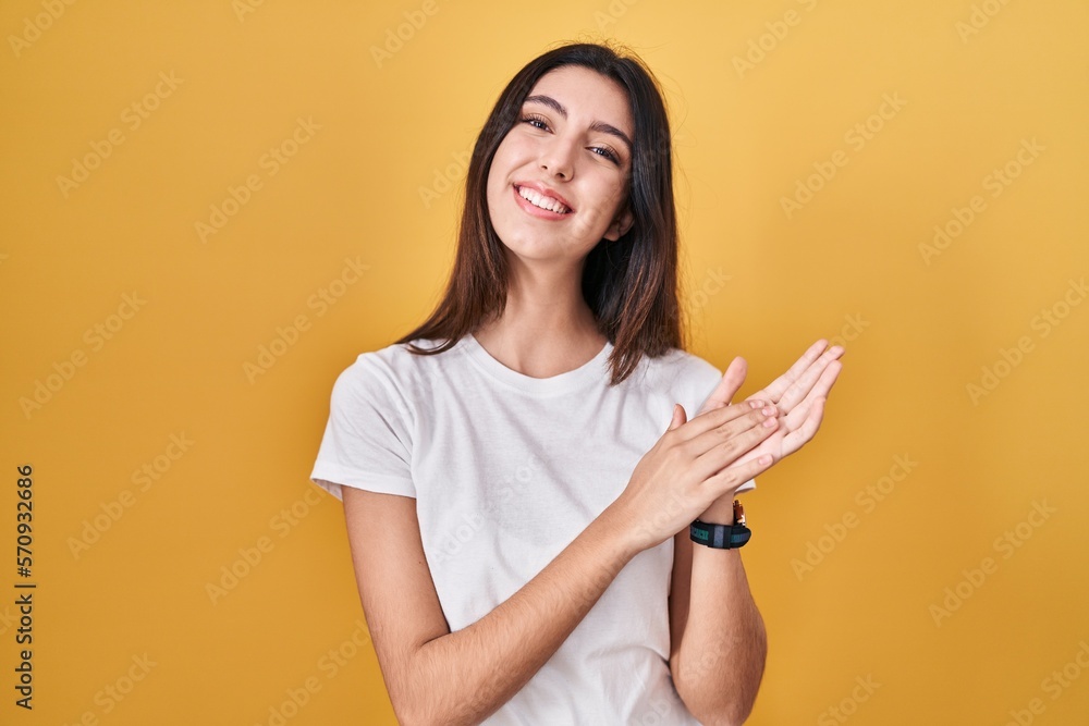 Young beautiful woman standing over yellow background clapping and applauding happy and joyful, smiling proud hands together Young beautiful woman standing over yellow background clapping and applauding happy and joyful, smiling proud hands together