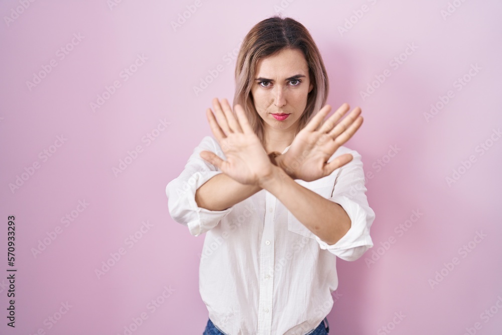 Young beautiful woman standing over pink background rejection expression crossing arms and palms doing negative sign, angry face Young beautiful woman standing over pink background rejection expression crossing arms and palms doing negative sign, angry face