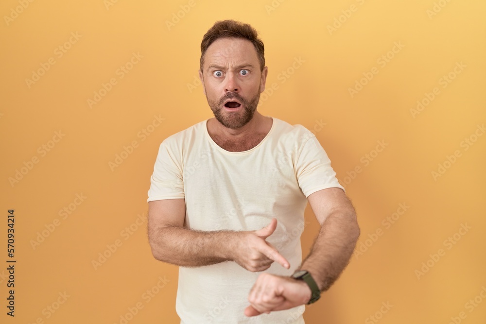 Middle age man with beard standing over yellow background in hurry pointing to watch time, impatience, upset and angry for deadline delay Middle age man with beard standing over yellow background in hurry pointing to watch time, impatience, upset and angry for deadline delay