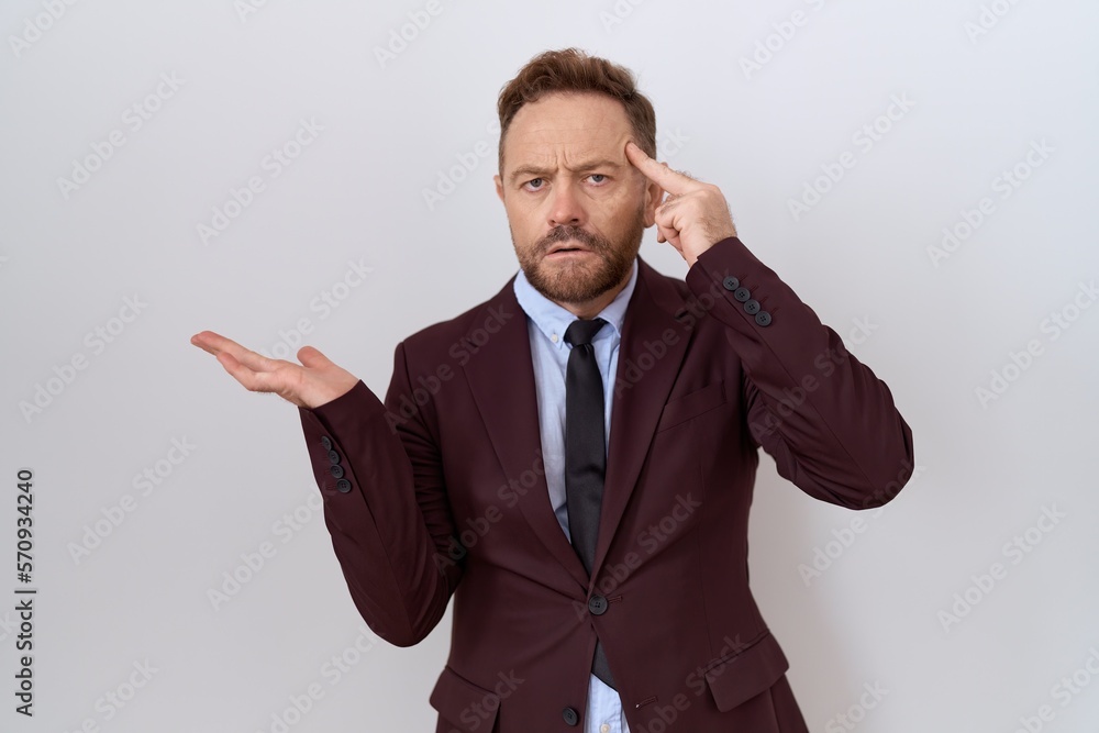 Middle age business man with beard wearing suit and tie confused and annoyed with open palm showing copy space and pointing finger to forehead. think about it. Middle age business man with beard wearing suit and tie confused and annoyed with open palm showing copy space and pointing finger to forehead. think about it.