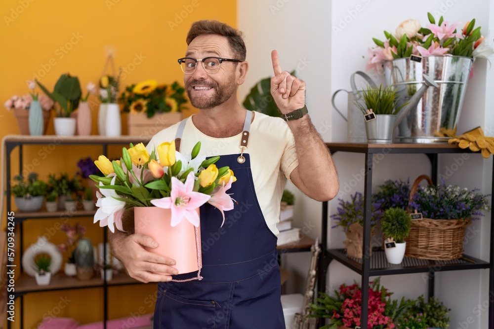 Middle age man with beard working at florist shop holding plant surprised with an idea or question pointing finger with happy face, number one Middle age man with beard working at florist shop holding plant surprised with an idea or question pointing finger with happy face, number one