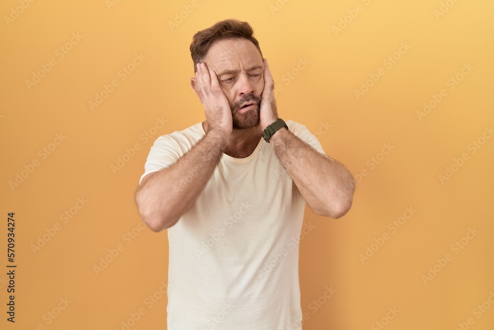 Middle age man with beard standing over yellow background tired hands covering face, depression and sadness, upset and irritated for problem Middle age man with beard standing over yellow background tired hands covering face, depression and sadness, upset and irritated for problem