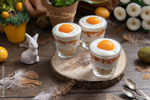 Ei im Glas geschichtet als Dessert zu Ostern auf Untergrund und Hintergrund aus Holz mit Blumen und Deko