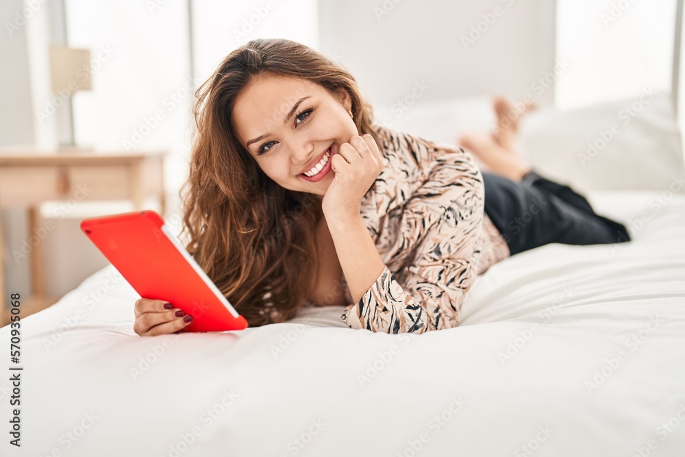 Young beautiful hispanic woman using touchpad lying on bed at bedroom Young beautiful hispanic woman using touchpad lying on bed at bedroom