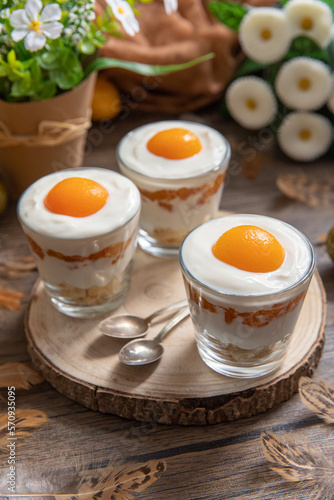 Ei im Glas geschichtet als Dessert zu Ostern auf Untergrund und Hintergrund aus Holz mit Blumen und Deko