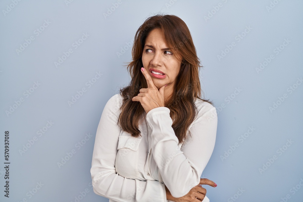 Hispanic woman standing over isolated background thinking worried about a question, concerned and nervous with hand on chin Hispanic woman standing over isolated background thinking worried about a question, concerned and nervous with hand on chin