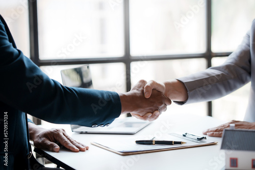 Real estate agent shakes hands with a client to sign a home purchase contract congratulating the client on the purchase.