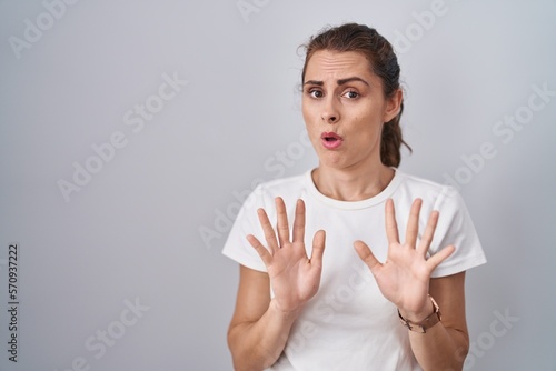 Beautiful brunette woman standing over isolated background moving away hands palms showing refusal and denial with afraid and disgusting expression. stop and forbidden. photo