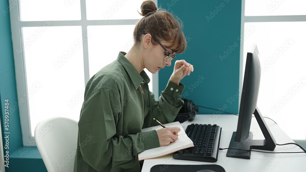 Young caucasian woman student using computer taking notes at library university