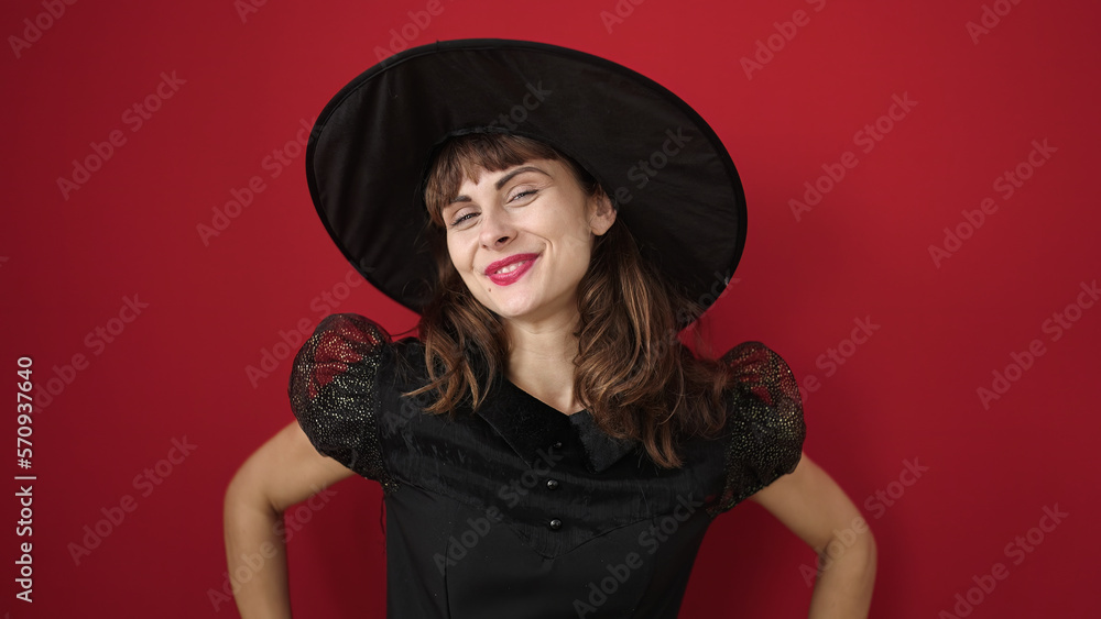 Young caucasian woman smiling wearing witch costume over isolated red background Young caucasian woman smiling wearing witch costume over isolated red background