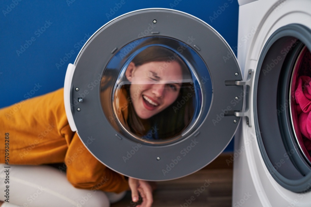 Young brunette woman looking through the washing machine window winking looking at the camera with sexy expression, cheerful and happy face. Young brunette woman looking through the washing machine window winking looking at the camera with sexy expression, cheerful and happy face.