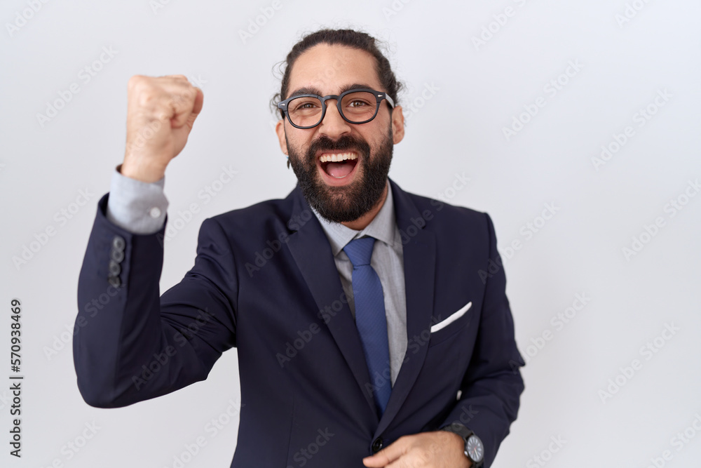 Hispanic man with beard wearing suit and tie angry and mad raising fist frustrated and furious while shouting with anger. rage and aggressive concept. Hispanic man with beard wearing suit and tie angry and mad raising fist frustrated and furious while shouting with anger. rage and aggressive concept.