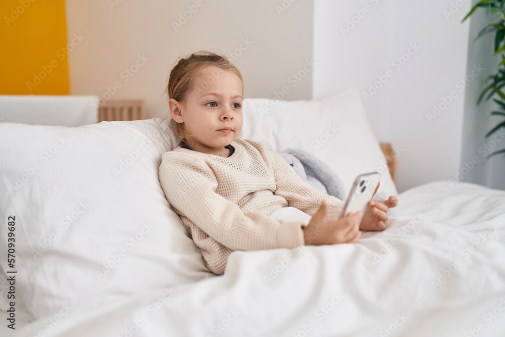 Adorable blonde girl using smartphone sitting on bed at bedroom Adorable blonde girl using smartphone sitting on bed at bedroom