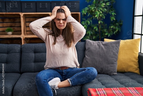 Beautiful woman sitting on the sofa at home suffering from headache desperate and stressed because pain and migraine. hands on head.